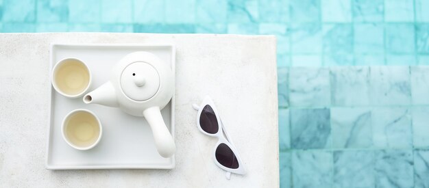 Witte zonnebril en hete theepot in de buurt van zwembad in luxehotel Zomerreis vakantie vakantie en weekend concept