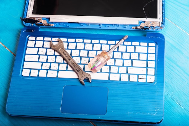 Wizard repairs laptop with tools and hands on the blue wooding table top view wrench and screwdriver on the keyboard top view Disassembly of the laptop into spare parts View of the laptop inside