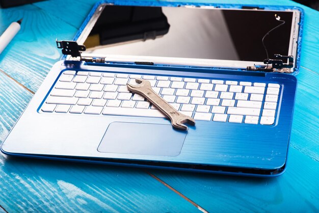 Wizard repairs laptop with tools and hands on the blue wooding table top view wrench and screwdriver on the keyboard top view Disassembly of the laptop into spare parts View of the laptop inside