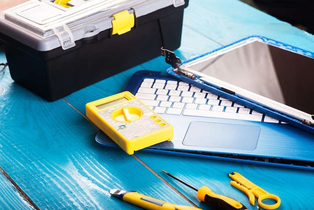 Wizard repairs laptop with tools and hands on the blue wooding table top view