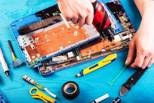 Wizard repairs laptop with tools and hands on the blue wooding table top view