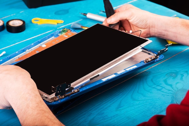 Wizard repairs laptop with tools and hands on the blue wooding table top view