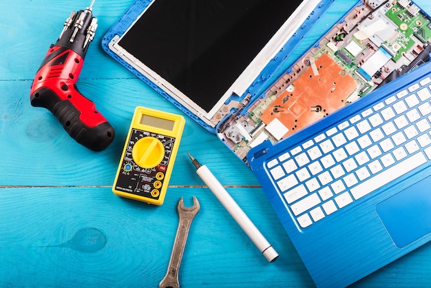 La procedura guidata ripara il computer portatile con gli strumenti e le mani sulla vista dall'alto del tavolo in legno blu