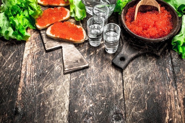 Foto wodka en sandwiches met rode kaviaar op houten tafel.