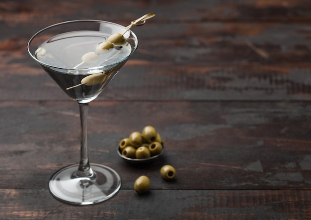 Wodka martini gin cocktail in origineel glas met olijven in metalen kom en bamboestokken op houten oppervlak. ruimte voor tekst