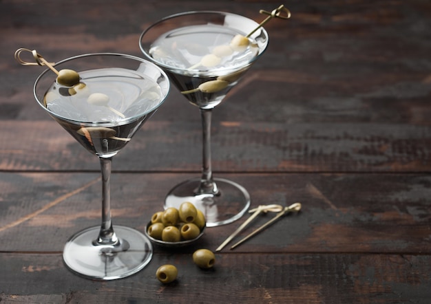 Wodka martini gin cocktail in originele glazen met olijven in metalen kom en bamboestokken op donkere houten ondergrond.