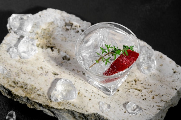 Wodka of gin in borrelglas met ijs versierd met aardbeischijfje en tijm op travertijnpodium