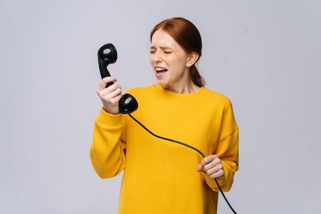 Woedende boze jonge vrouw in stijlvolle gele trui praten over retro telefoon en schreeuwen in handset