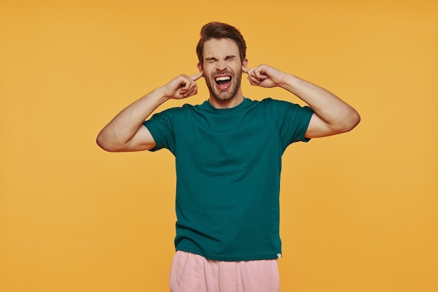 Woedende jongeman in casual kleding die een gezicht trekt terwijl hij tegen de gele muur staat