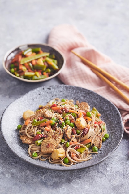 Foto wok con carne di tacchino soba noodles mais piselli fagiolini e carote serviti su sfondo grigio