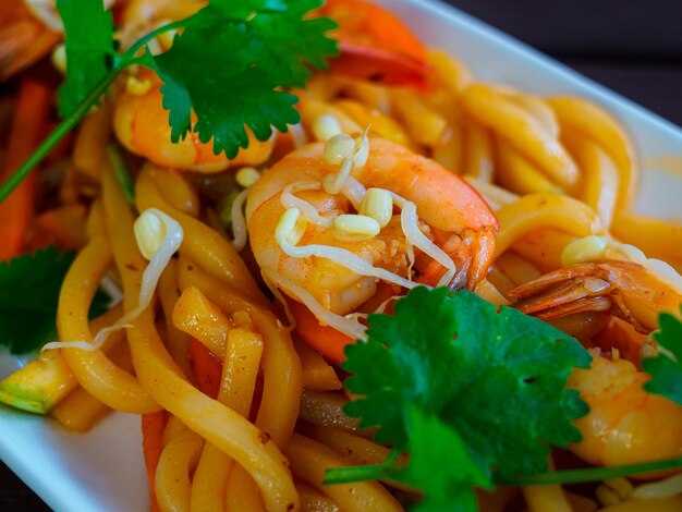 Wok with udon noodles king prawns sprouted white mung beans garnished with sprigs of green cilantro