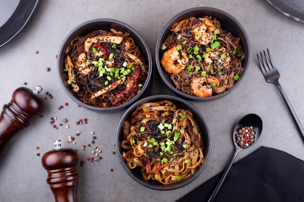 Woknoedels met garnalen, in een zwarte plaat versierd met erwten, op een grijze achtergrond. Het concept van de Aziatische keuken.
