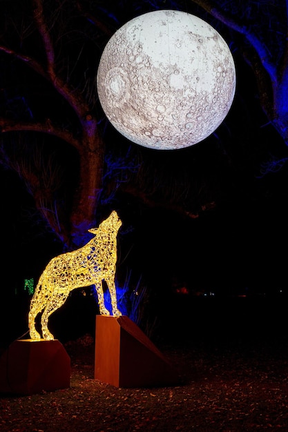 Foto una statua di lupo è esposta con una grande luna piena dietro di essa