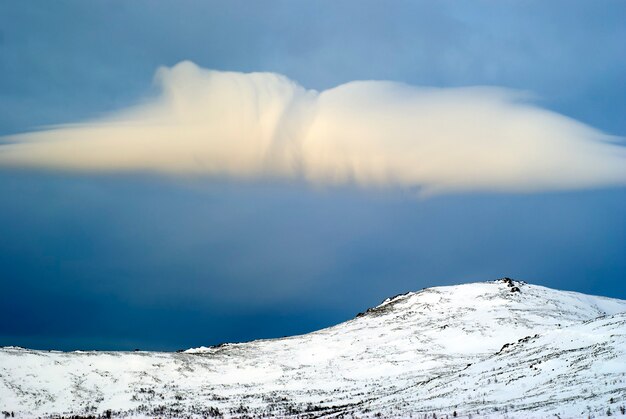 Wolk boven een besneeuwde bergtop; ochtendlandschap in de buurt van de berg Konzhakovskiy Kamen