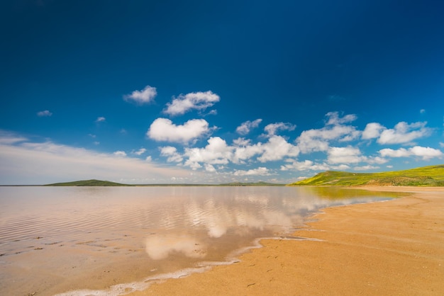 Foto wolken in de blauwe lucht worden weerspiegeld in het water op de zandige kust