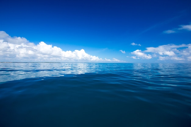 Wolken op blauwe lucht boven kalme zee met reflectie van zonlicht