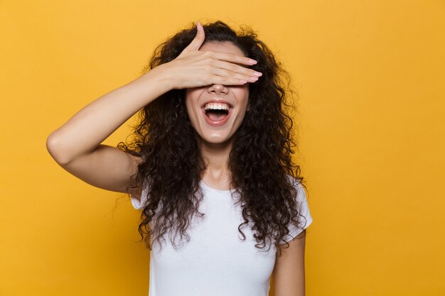 woman 20s with curly hair smiling and coning eyes with palm isolated on yellow