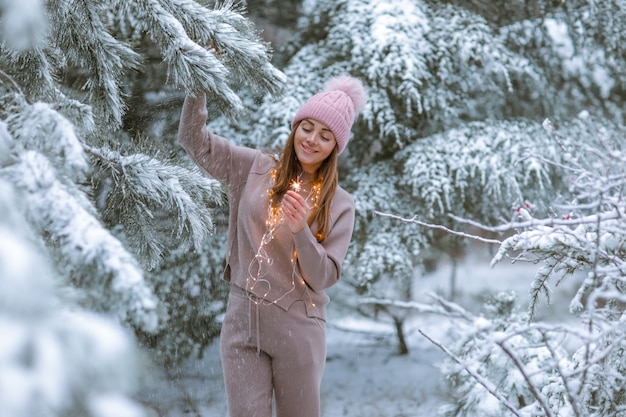 Woman 30-35 years old in a warm tracksuit on the background of a snowy forest with Christmas trees