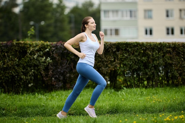 Donna anni '30 che fa jogging nel parco estivo vicino a una zona residenziale con condomini