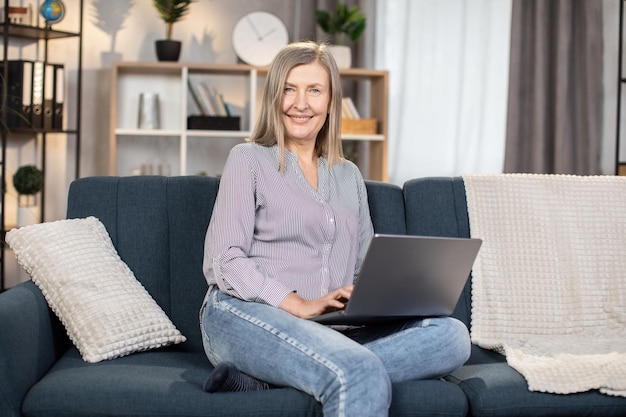 Woman of 60s resting on couch with portable laptop