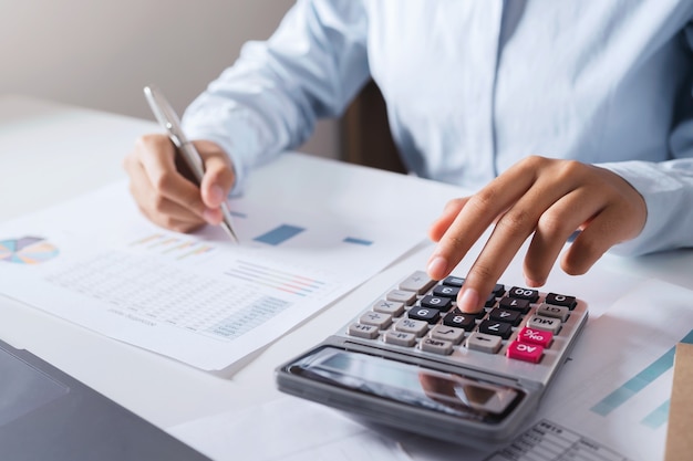 Woman accountant use calculator and computer with holding pen on desk in office