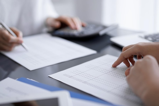 Woman accountant using a calculator and laptop computer while counting and discussing taxes with a client. Business audit concepts