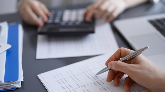 Женщина-бухгалтер, использующая калькулятор и ноутбук при подсчете налогов для клиента.