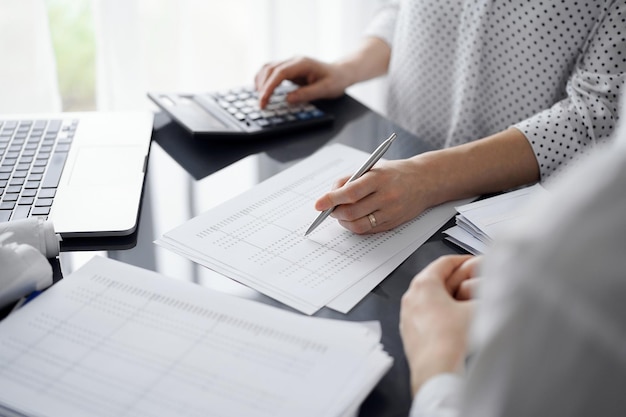 Woman accountant using a calculator and laptop computer while counting taxes for a client. Business audit and finance concepts.