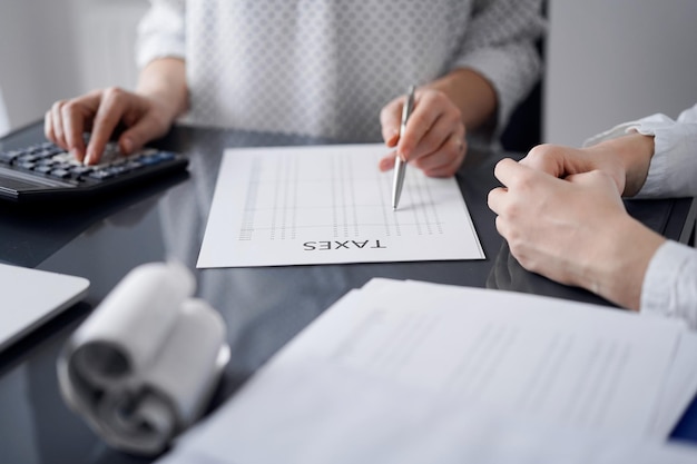 Woman accountant using a calculator and laptop computer while counting taxes for a client. Business audit and finance concepts.