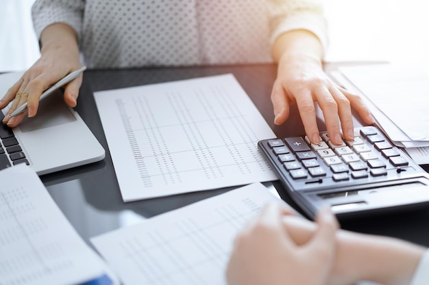 Woman accountant using a calculator and laptop computer while counting taxes with a client or a colleague. Business audit team, finance advisor