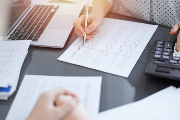 Woman accountant using a calculator and laptop computer while counting taxes with a client or a colleague. Business audit team, finance advisor.