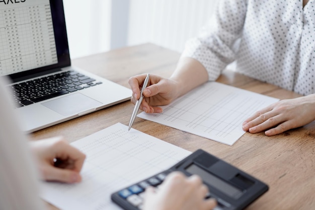 Woman accountant using a calculator and laptop computer while counting taxes with colleague at wooden desk in office. Teamwork, business audit and finance concepts.