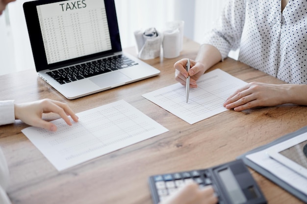 Photo woman accountant using a calculator and laptop computer while counting taxes with colleague at wooden desk in office. teamwork in business audit and finance