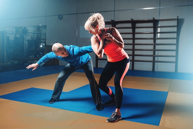 Woman in actoin on self-defense training with personal instructor, fighting workout in gym, martial art