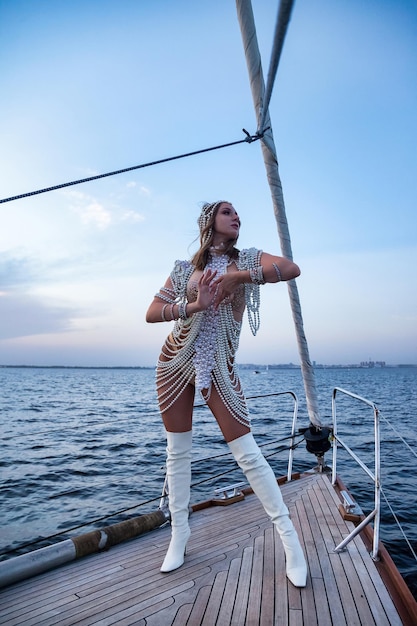 Woman actress in white stage costume full body posing on yacht at sea and blue sky background Female in theatre clothes outdoors