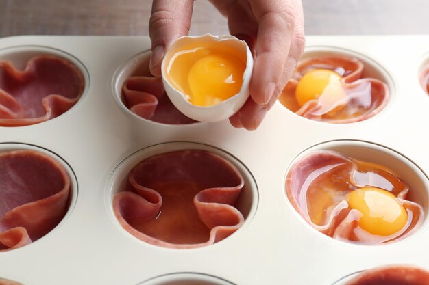 woman adding egg into muffin tin with ham closeup
