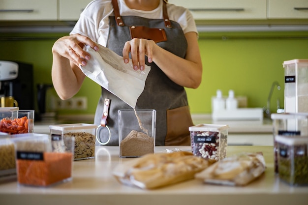 Woman adding healthy pea pasta into transparent box storage organization at kitchen