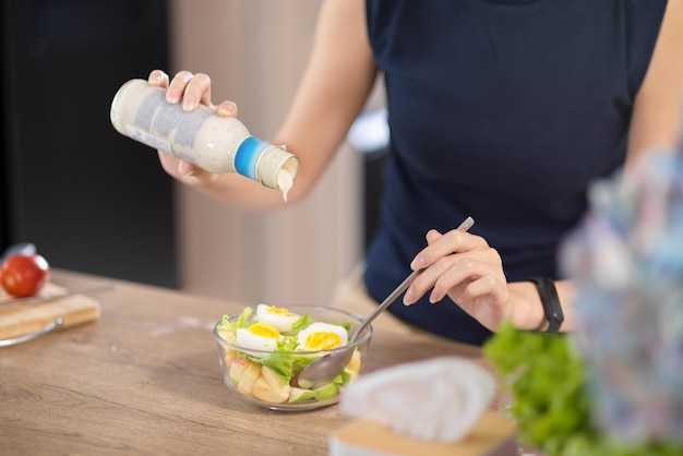 A woman adding salad dressing in her healthy salad bowl home cooking healthy and diet food concept