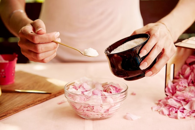 Donna che aggiunge zucchero ai petali di rosa per la marmellata naturale marmellata organica fatta in casa estetica che si prepara con petali di rosa del tè fotografia di stile di vita