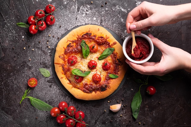 Woman adding tomato sauce to freshly baked pizza