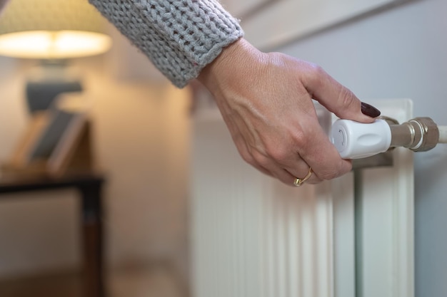 Woman adjusting temperature on heating radiator Energy crisis concept in Europe Rising costs in private households for gas bill due to inflation and war