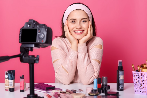 Woman advertises new beauty products, makes video her blog. Beauty vlogger sits smilling in front of camera