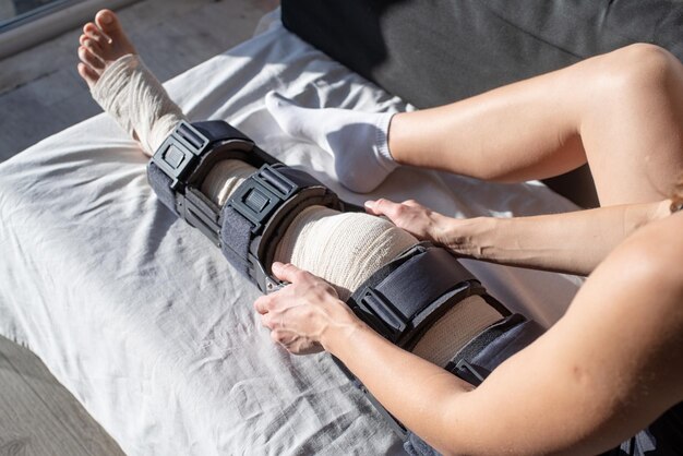 Woman after car accident in an orthosis sitting on couch female fastening knee orthosis