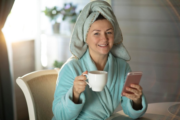 コーヒーのマグカップと電話で朝シャワーを浴びた後の女性