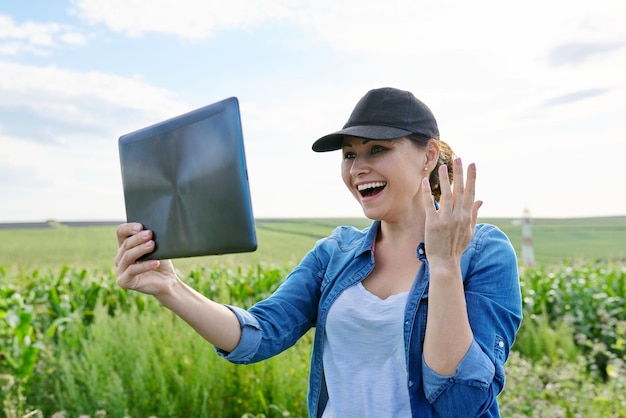 Woman agricultural worker inspecting corn field video call using digital tablet