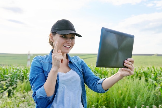 Woman agricultural worker inspecting corn field video call using digital tablet