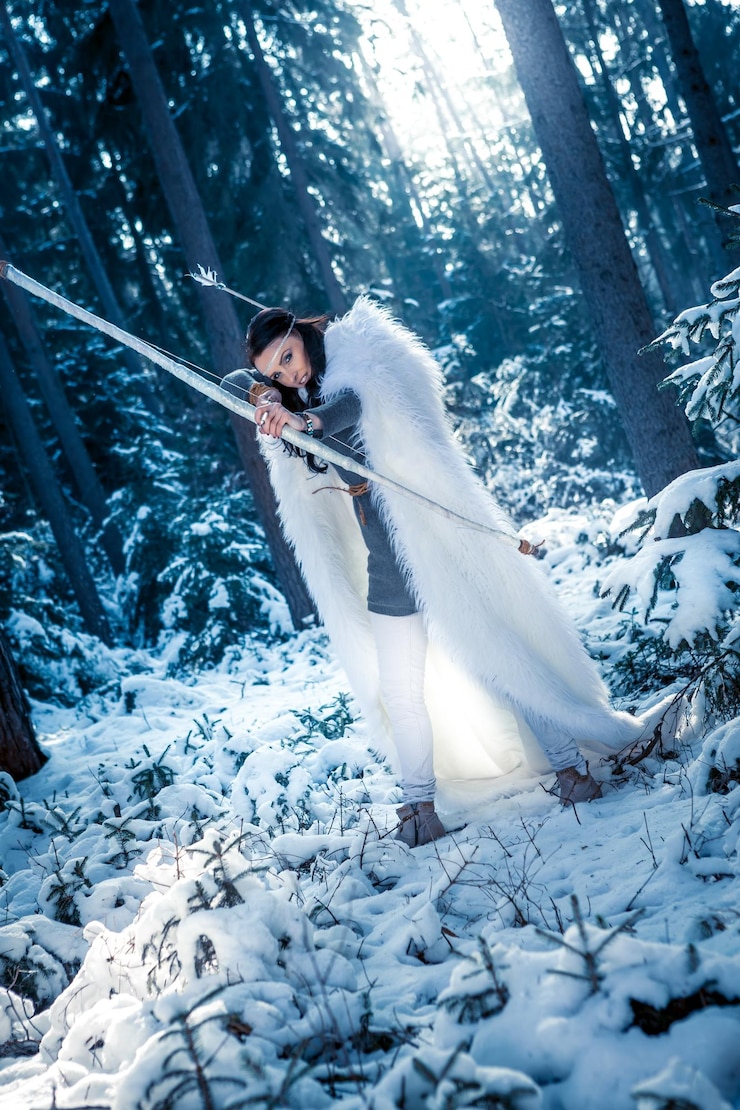 Photo woman aiming archery while standing on snow covered field against trees in forest