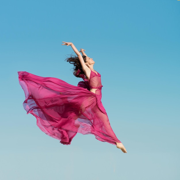 Woman in airy red dress jumping in the air