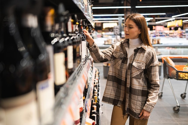 Женщина в алкогольном отделе супермаркета смотрит на полку с винами