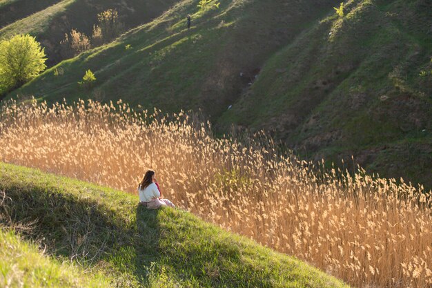 A woman alone enjoys the silence and beauty of nature, sitting on a hill in a picturesque place